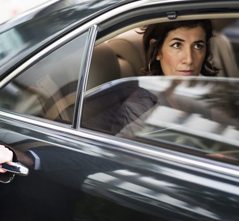 Professional woman looking out the tinted window of a luxury black car, emphasizing privacy and security.